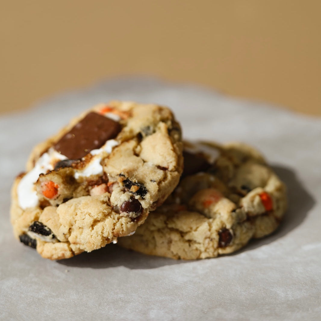 A cookie with a marshmallow crème filling, peanut butter chips, Reeses cups, Oreos, and mini marshmallows topped with chocolate covered graham crackers.